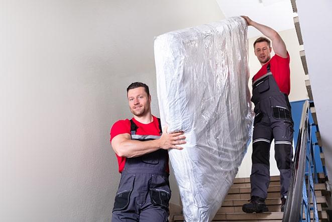 man carrying a heavy box spring out of a room in Palmyra